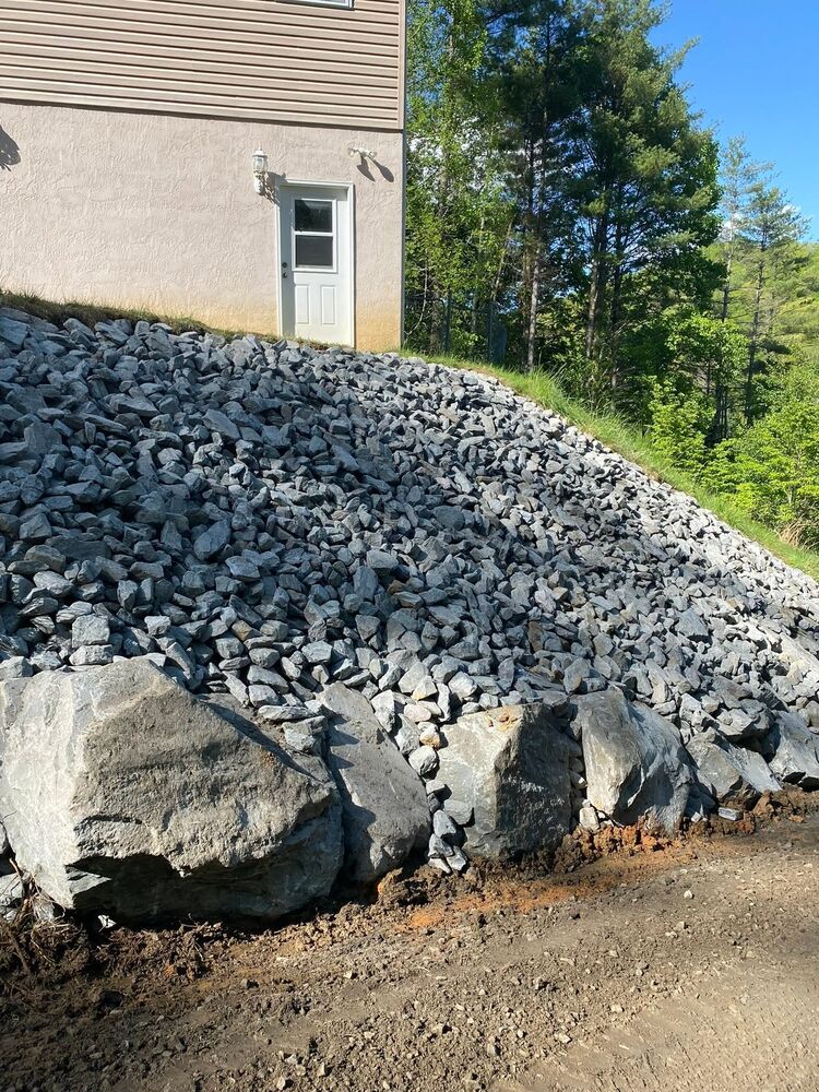 A large riprap stone bank armoring a steep slope beside a house