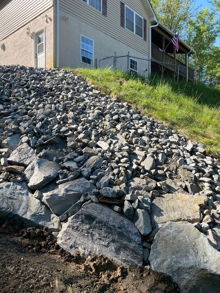 Large riprap boulders set into a slope to hold the bank by a house